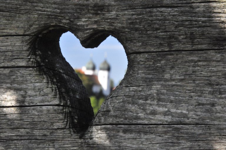 Holzbrett mit Herzausschnitt, dahinter Kirchtürme