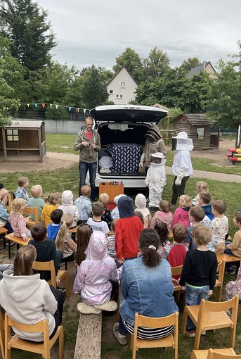 Kinder lauschen aufmerksam den Erklärungen eines Imkers
