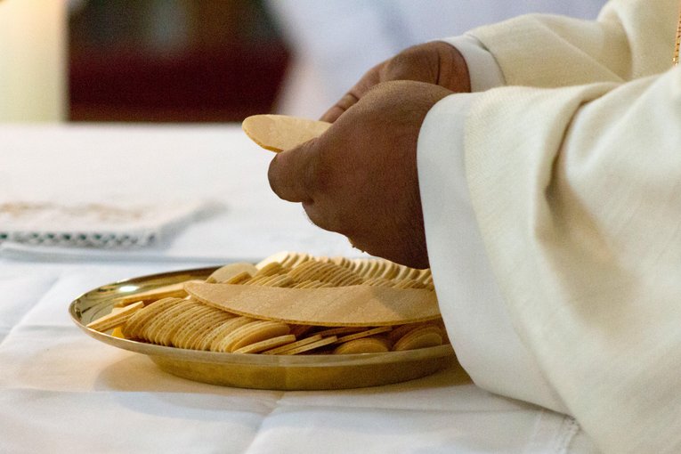 Hände eines Priesters mit Hostie während Eucharistie, Schale mit Hostien auf dem Altar