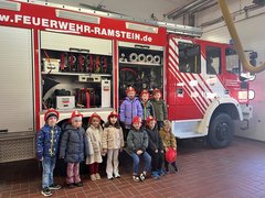 10 Kindergartenkinder mit Feuerwehrhelm vor einem Feuerwehrauto in einer Halle
