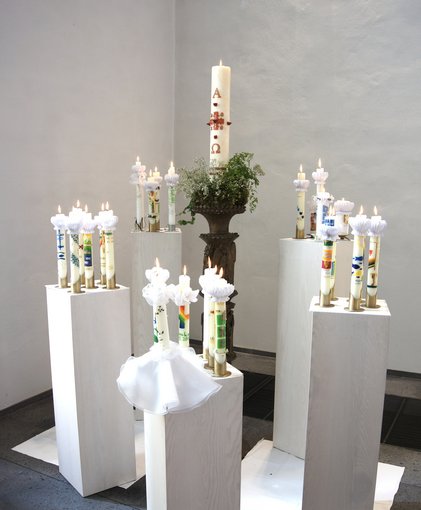 verschiedene Kommunionkerzen auf 5 Stelen um eine Osterkerze gruppiert